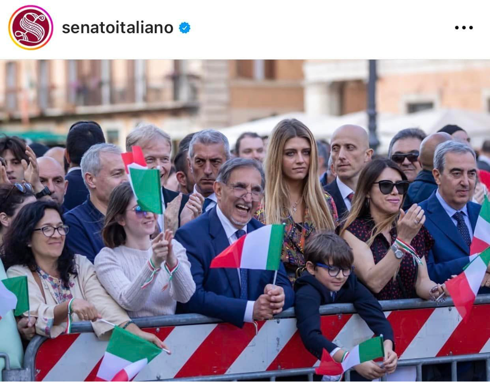 presidente del senato La Russa che sventola una bandierina italiana assieme ad altre persone, ed al Senatore Malan, mentre assistono alla festa del settantacinquesimo anniversario del senato